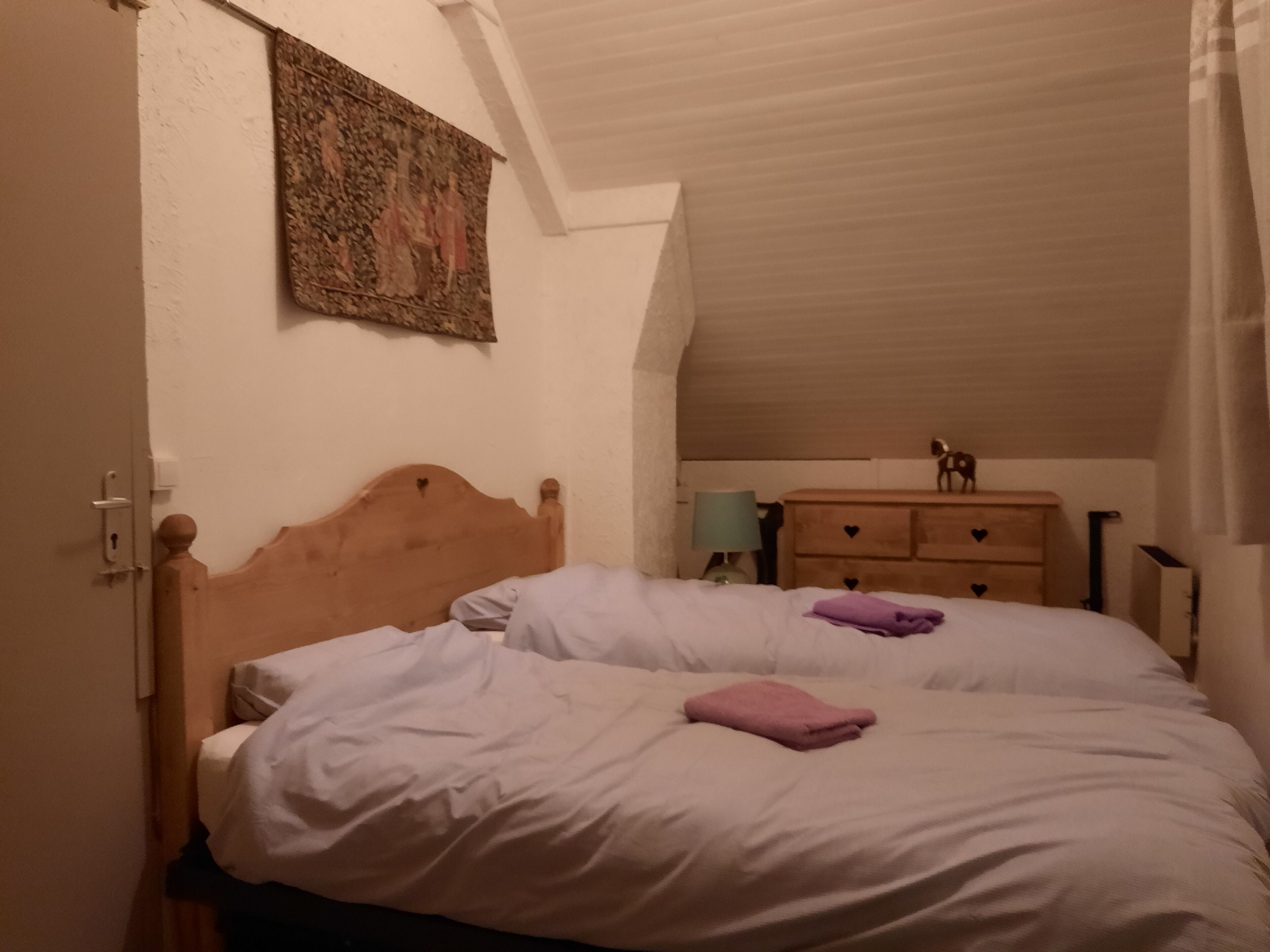 A bedroom with two beds, a wooden headboard, a dresser with heart-shaped handles, a tapestry on the wall, and a small statue on the dresser.