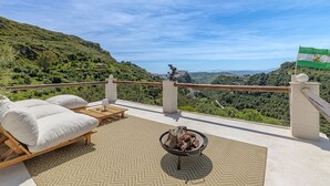 Una terraza con vistas a un valle verde, una bandera y una hoguera.