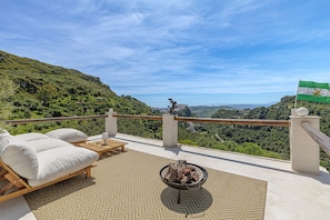 Eine Terrasse mit Blick auf ein grünes Tal, einer Flagge und einer Feuerstelle.