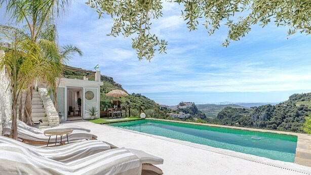 Zona de piscina con sillones reclinables, una escalera de piedra y vistas a un pueblo en la ladera.