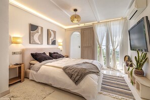 Ein modernes Schlafzimmer mit einem großen Bett, Nachttischlampen, einem Fernseher und Blick ins Freie.