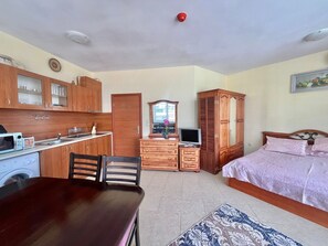 Ein kleines Zimmer mit Küchenzeile, einem Bett, einem Schminktisch und einem Spiegel.