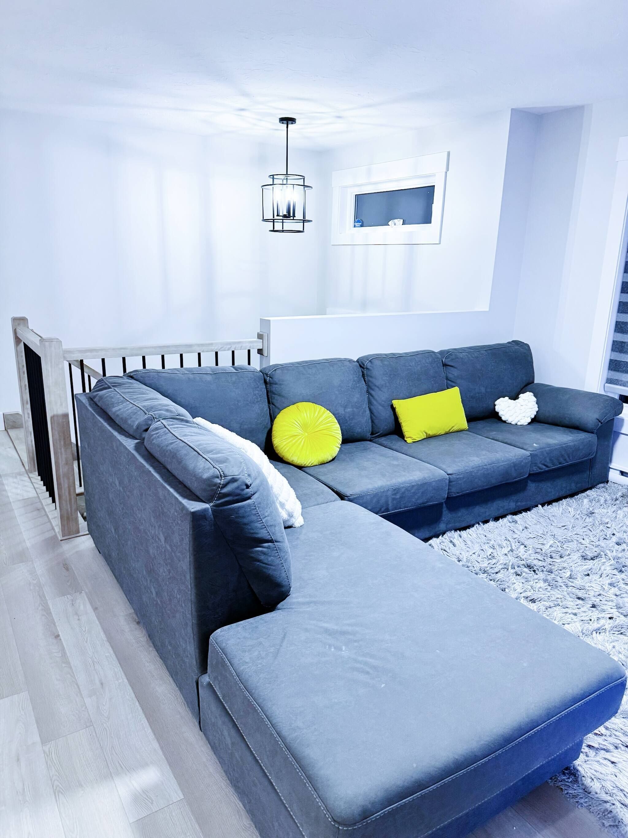 A modern living room with a sectional sofa, a small ottoman, a white radiator, a grey rug, and a hanging light fixture.
