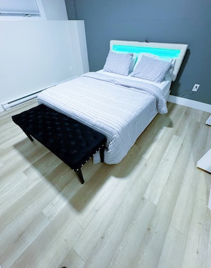 A bedroom with a bed, a bench, a wall socket, and a radiator. - Wonderful 3-bedroom Full House Near Magnetic Hill (Moncton)