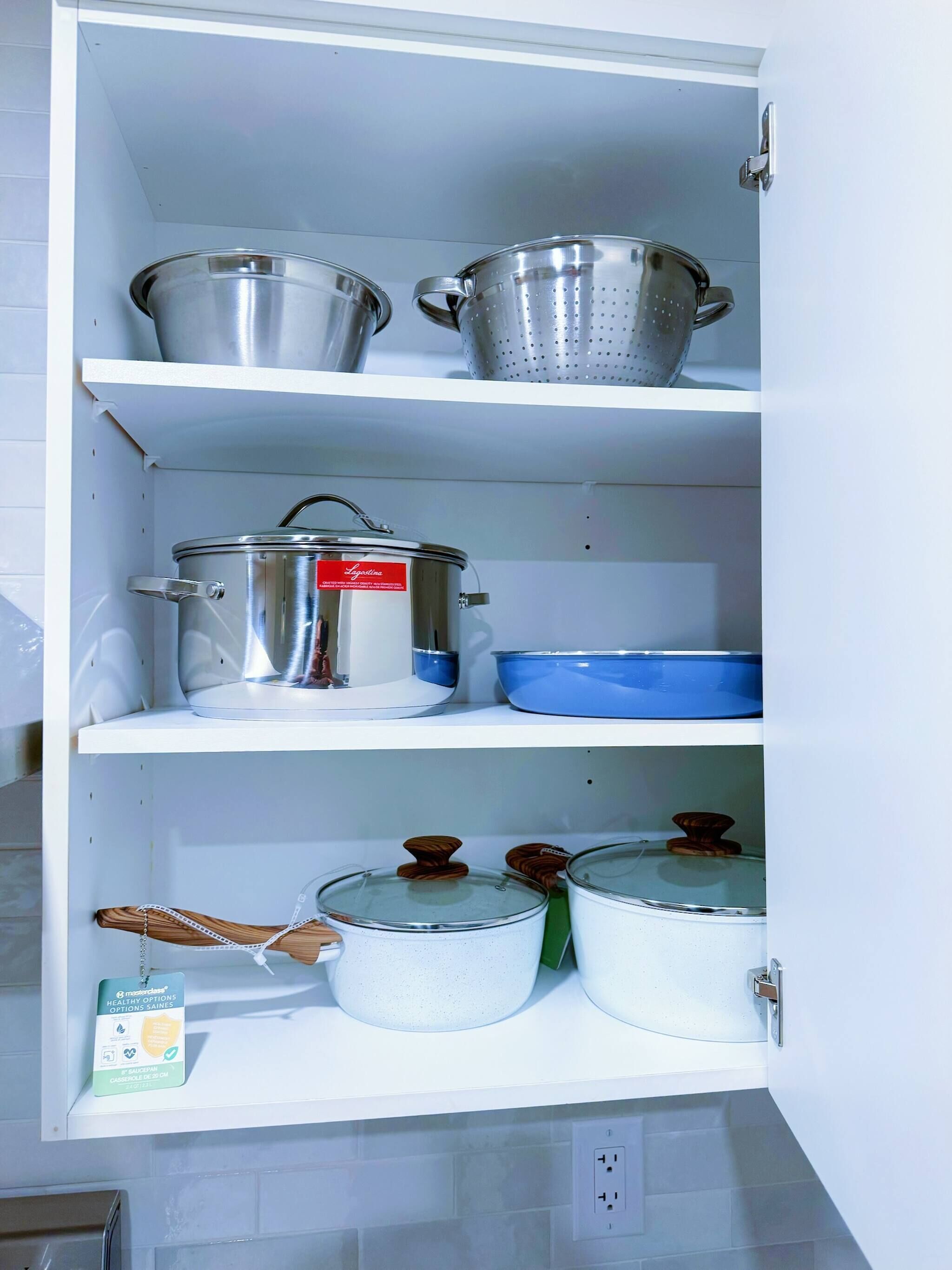 A kitchen with stainless steel pots and pans on shelves, a blue baking dish, and a wooden spoon.