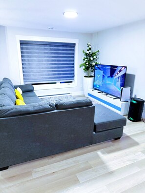 En moderne stue med en grå sofa, et fladskærms-tv, en Sony-højttaler og en potteplante.