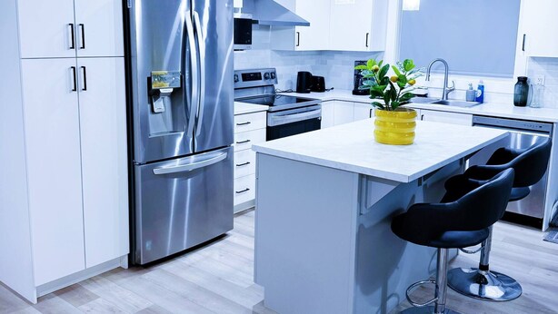 A modern kitchen with white cabinets, stainless steel appliances, a central island with bar stools, and pendant lighting. - Wonderful 3-bedroom Full House Near Magnetic Hill (Moncton)