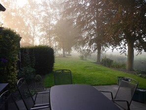 A patio area with a table and chairs, surrounded by greenery and trees. - Dike house with a view (Wilhelmshaven)