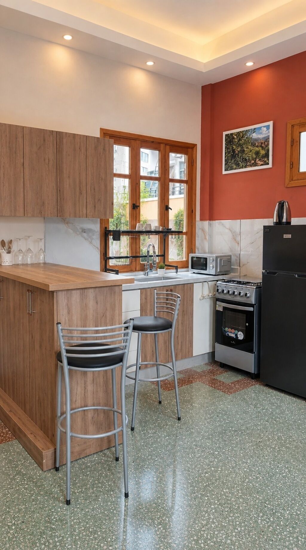 A kitchen with wooden cabinets, a countertop, a sink, a stove, a refrigerator, and two bar stools.