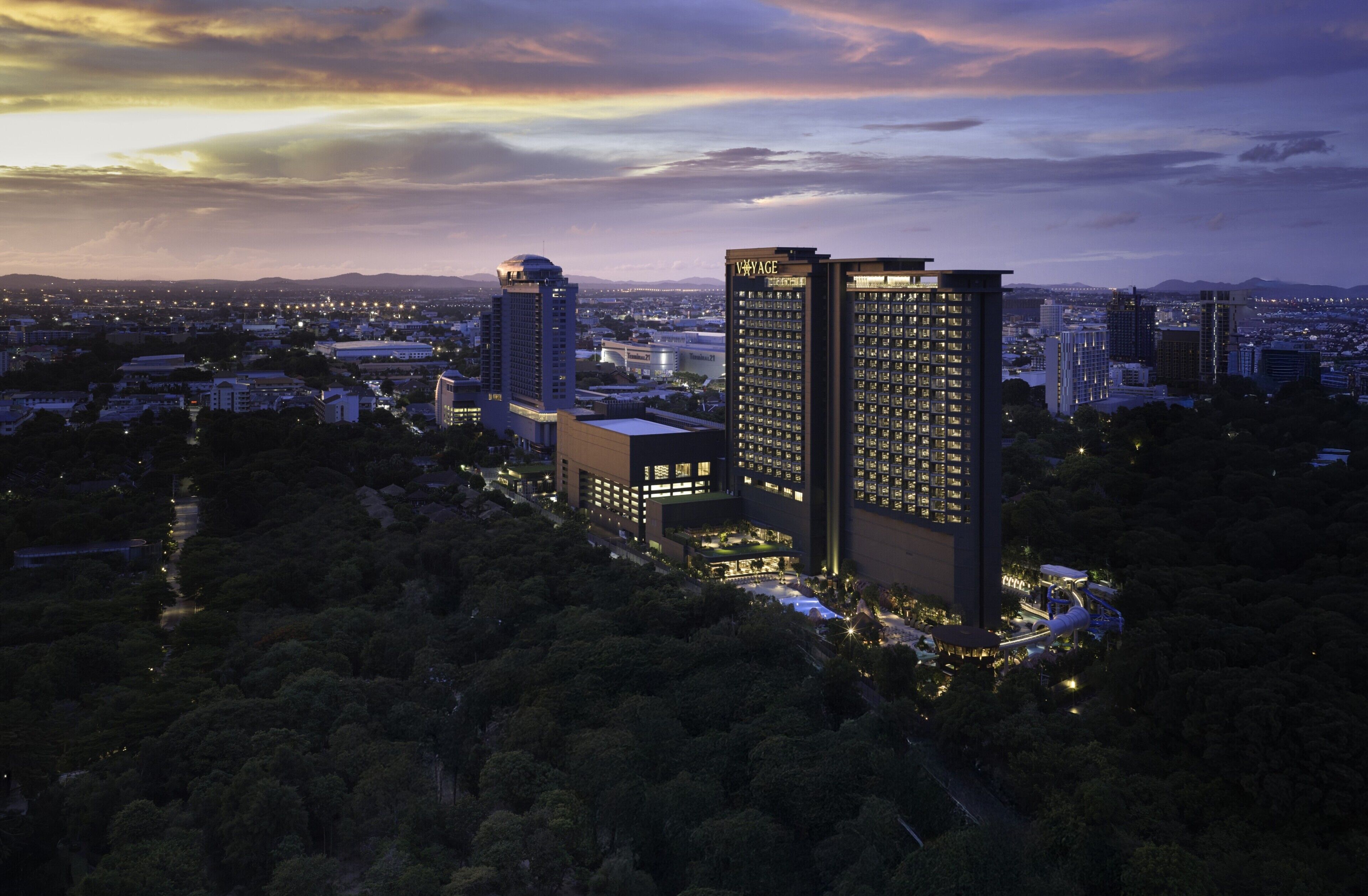 A high-rise hotel with multiple floors, surrounded by dense greenery and other buildings.