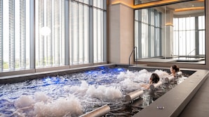 A spa area with a hot tub, large windows, and a view of the city. - Grande Centre Point Voyage Pattaya (Pattaya)