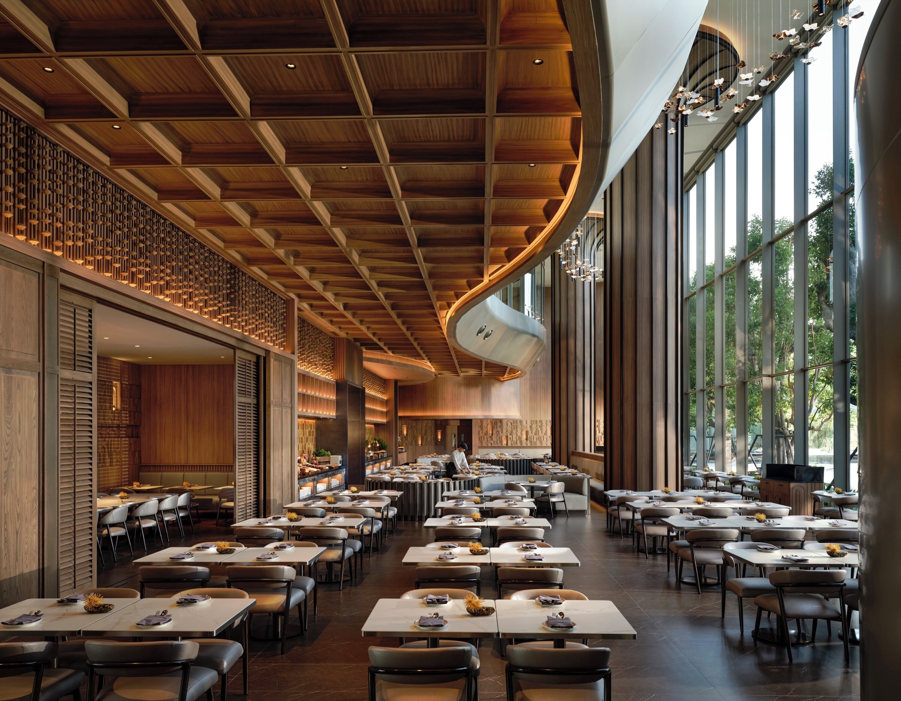A spacious restaurant with high ceilings, wooden paneling, and large windows. Tables are neatly arranged with chairs.