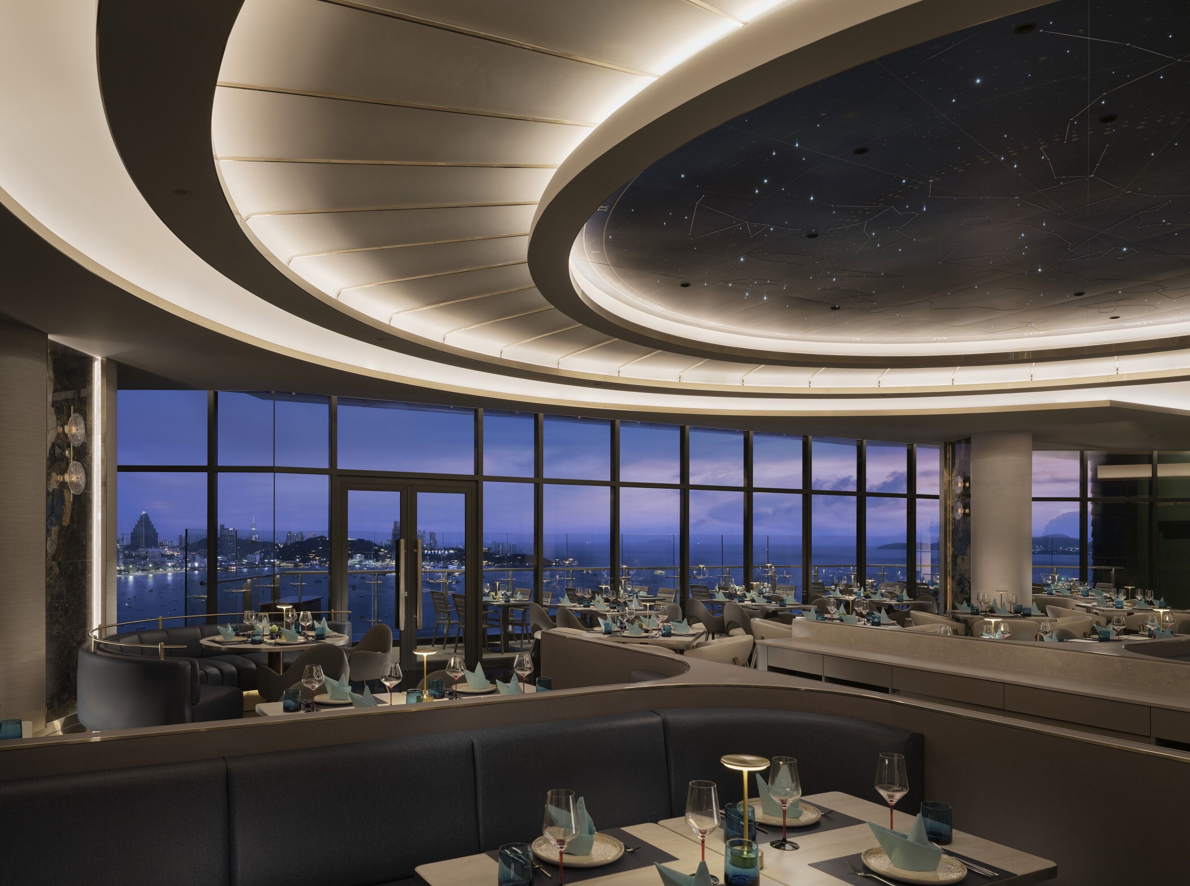 Un restaurante moderno con vistas panorámicas de la ciudad, que cuenta con un techo curvo con diseño de estrellas y un espacio amplio.