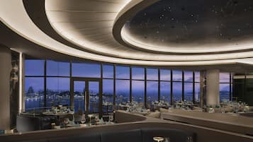 Un restaurante moderno con vistas panorámicas de la ciudad, que cuenta con un techo curvo con diseño de estrellas y un espacio amplio.