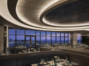 A modern restaurant with a panoramic city view, featuring a curved ceiling with a starry design and a spacious layout. - Grande Centre Point Voyage Pattaya (Pattaya)