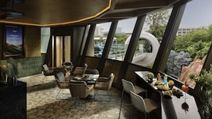 A restaurant with a modern interior, featuring a stone-tiled floor, wicker furniture, and large windows offering a view of the cityscape and greenery. - Grande Centre Point Voyage Pattaya (Pattaya)