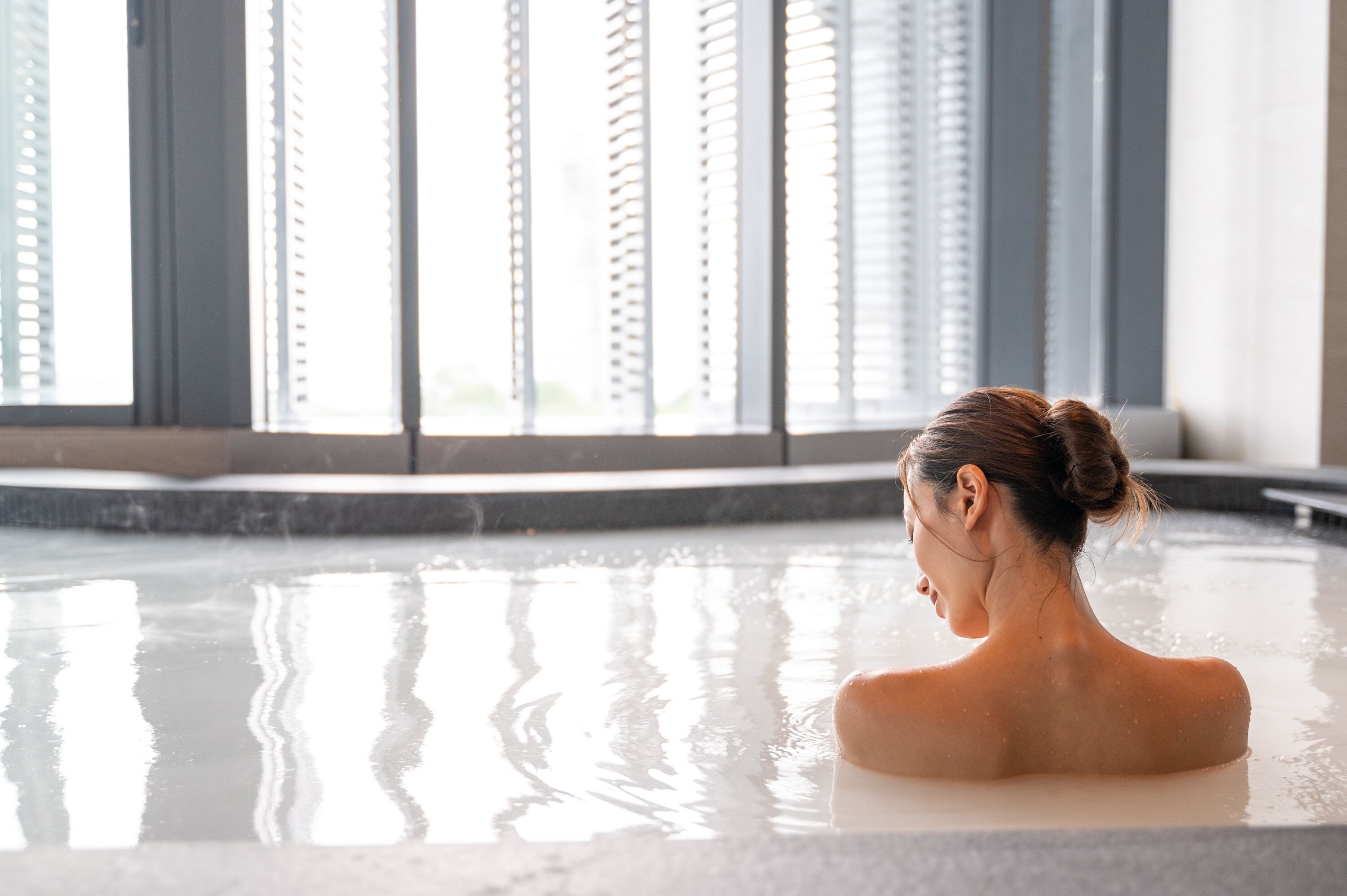 A person in a hot tub with a view of a building with large windows.