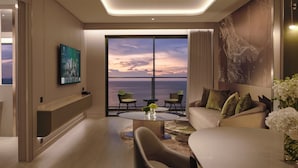 A modern living room with a large window offering a view of the sea, a flat-screen TV mounted on the wall, and a sofa with decorative pillows. - Grande Centre Point Voyage Pattaya (Pattaya)