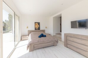 A bedroom with a bed, a TV, a painting, and a window.