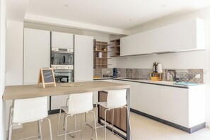 A modern kitchen with a central island, bar stools, a built-in oven, and a chalkboard sign.