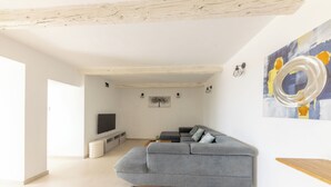 Ein modernes Wohnzimmer mit einem grauen Ecksofa, einem Flachbildfernseher und abstrakten Wandbildern.