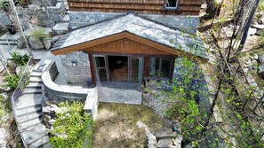 Une maison moderne avec une façade en pierre, un toit en bois et une porte d’entrée en verre.