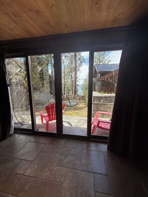 Et værelse med stor skydedør, der fører ud til en terrasse med røde stole og en stenvæg.