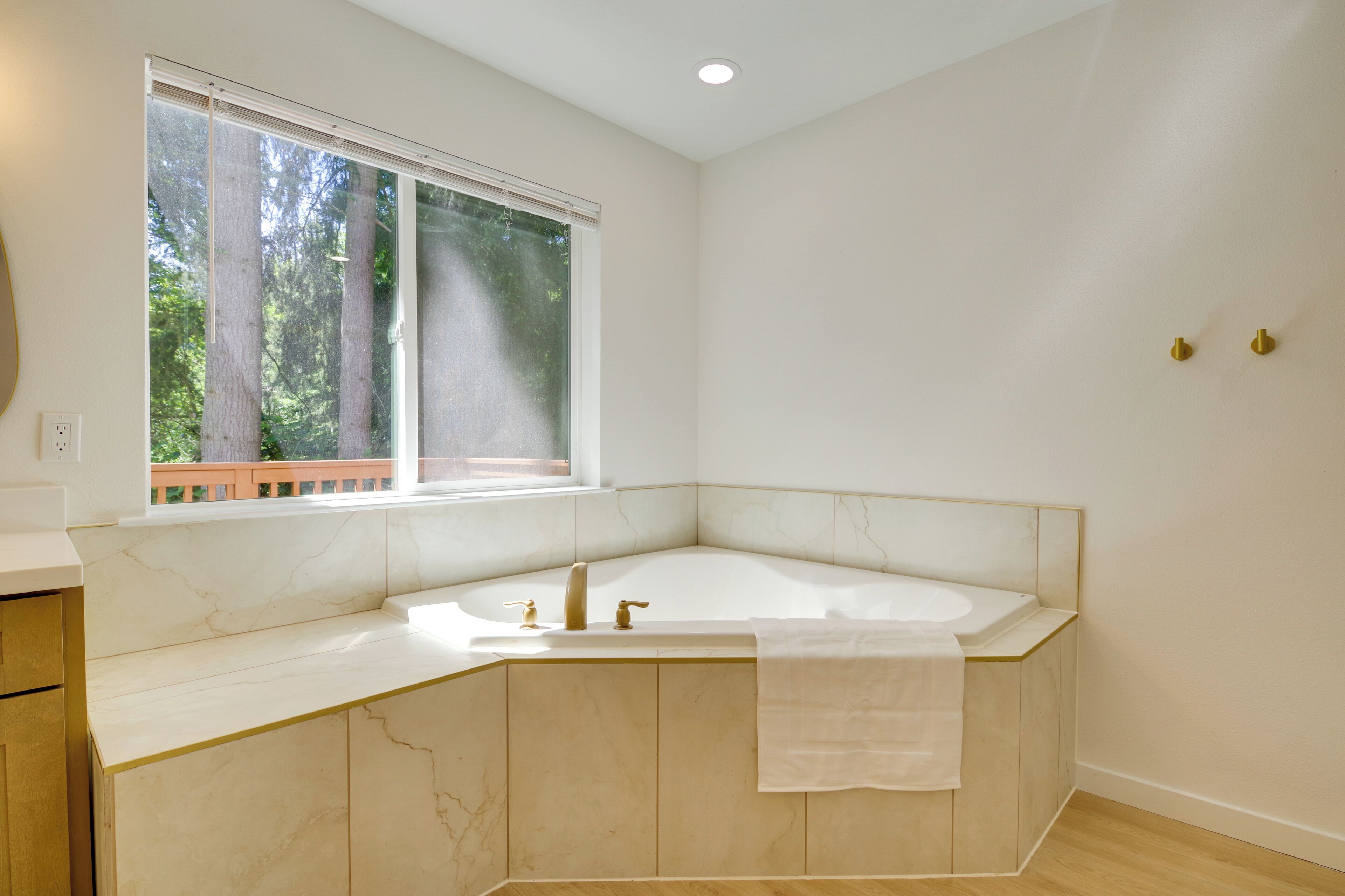 A modern bathroom with a freestanding bathtub, a window with a view of trees, and a marble countertop.