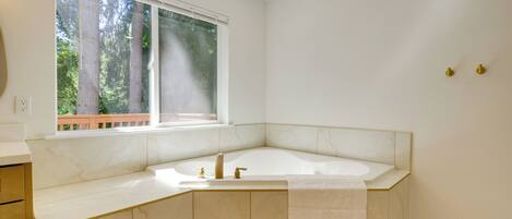 A modern bathroom with a freestanding bathtub, a window with a view of trees, and a marble countertop.