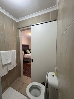 A small bathroom with a toilet, a towel rack, and a shower area. - Accommodation 8 Klein Straat Green (Paarl)