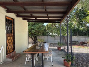 A covered patio with a wooden table and white chairs, surrounded by potted plants and a metal fence. - Accommodation 8 Klein Straat Green (Paarl)
