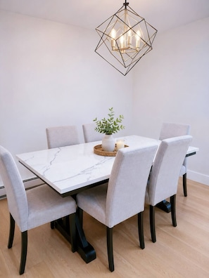 A dining table with six chairs, a geometric chandelier, and a small plant centerpiece. - Stylish 3-bedroom Full House Near Magnetic Hill (Moncton)