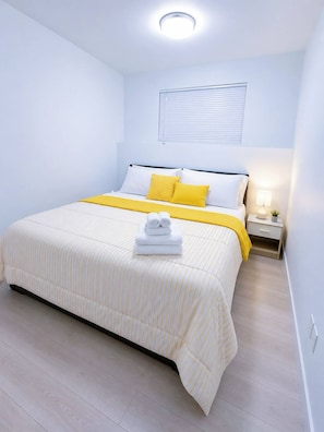 A neatly arranged hotel room with a bed, bedside table, lamp, and a window with blinds. - Stylish 3-bedroom Full House Near Magnetic Hill (Moncton)