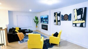 Ein modernes Wohnzimmer mit einer Couch, zwei gelben Sesseln, einem Flachbildfernseher und Kunstwerken an den Wänden.