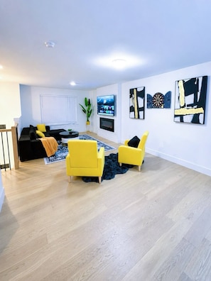 A modern living room with a sofa, two yellow armchairs, a flat-screen TV, and artwork on the walls. - Stylish 3-bedroom Full House Near Magnetic Hill (Moncton)