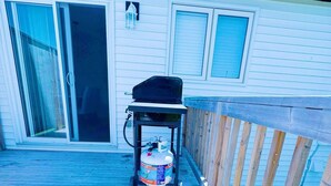 Eine Terrasse mit Grill, Propangasflasche, einer Schiebetür und einem Holzgeländer.