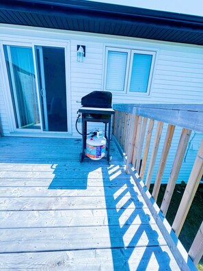 A deck with a grill and propane tank, a sliding glass door, and a wooden railing. - Stylish 3-bedroom Full House Near Magnetic Hill (Moncton)