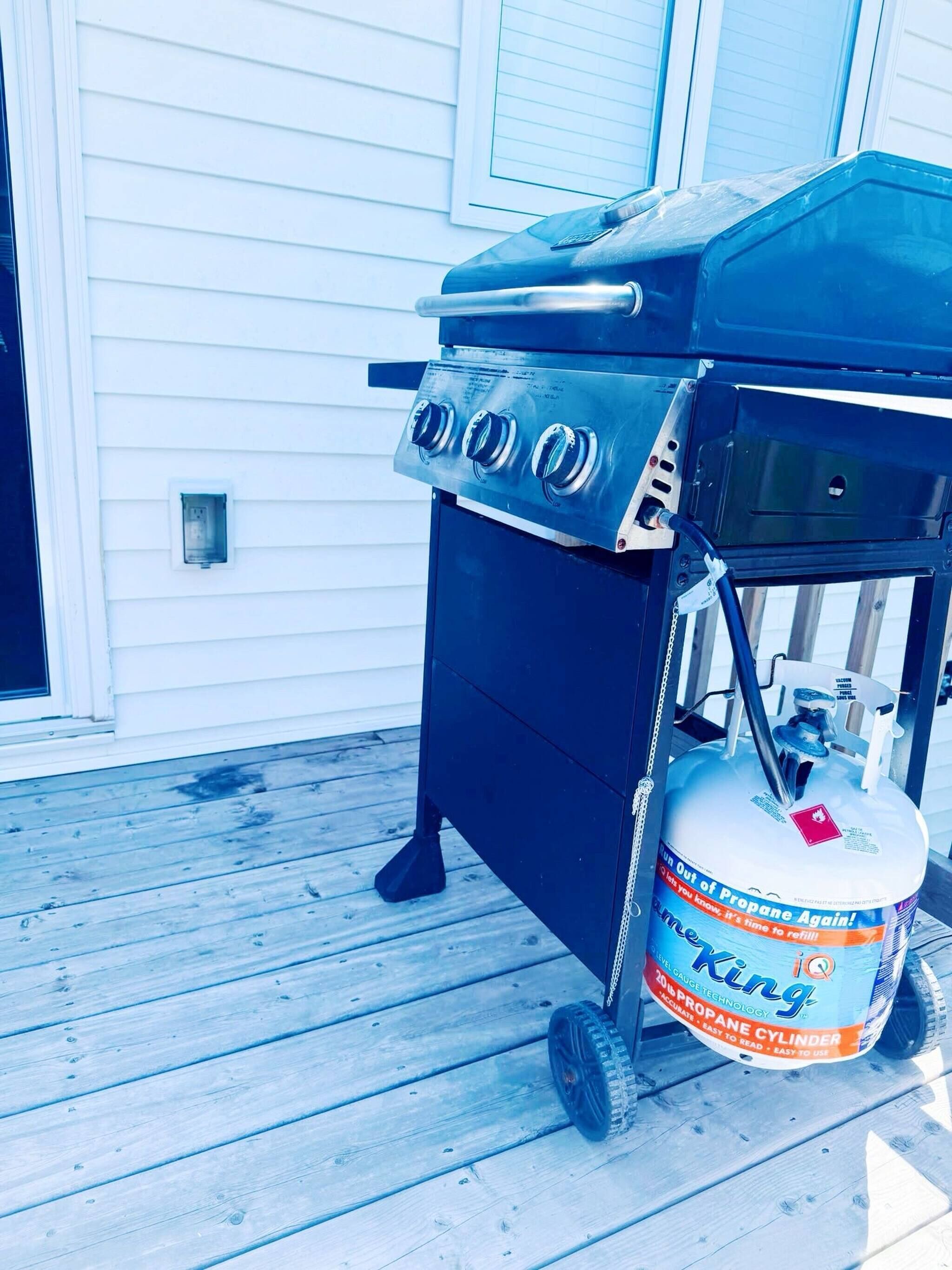 A propane grill with a propane tank on a wooden deck.
