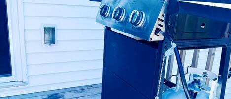 A propane grill with a propane tank on a wooden deck.