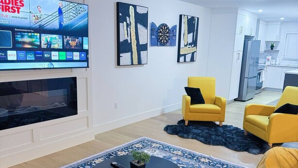 Ein modernes Wohnzimmer mit Flachbildfernseher, gelben Sesseln, einem schwarzen Couchtisch und abstrakter Wandkunst.