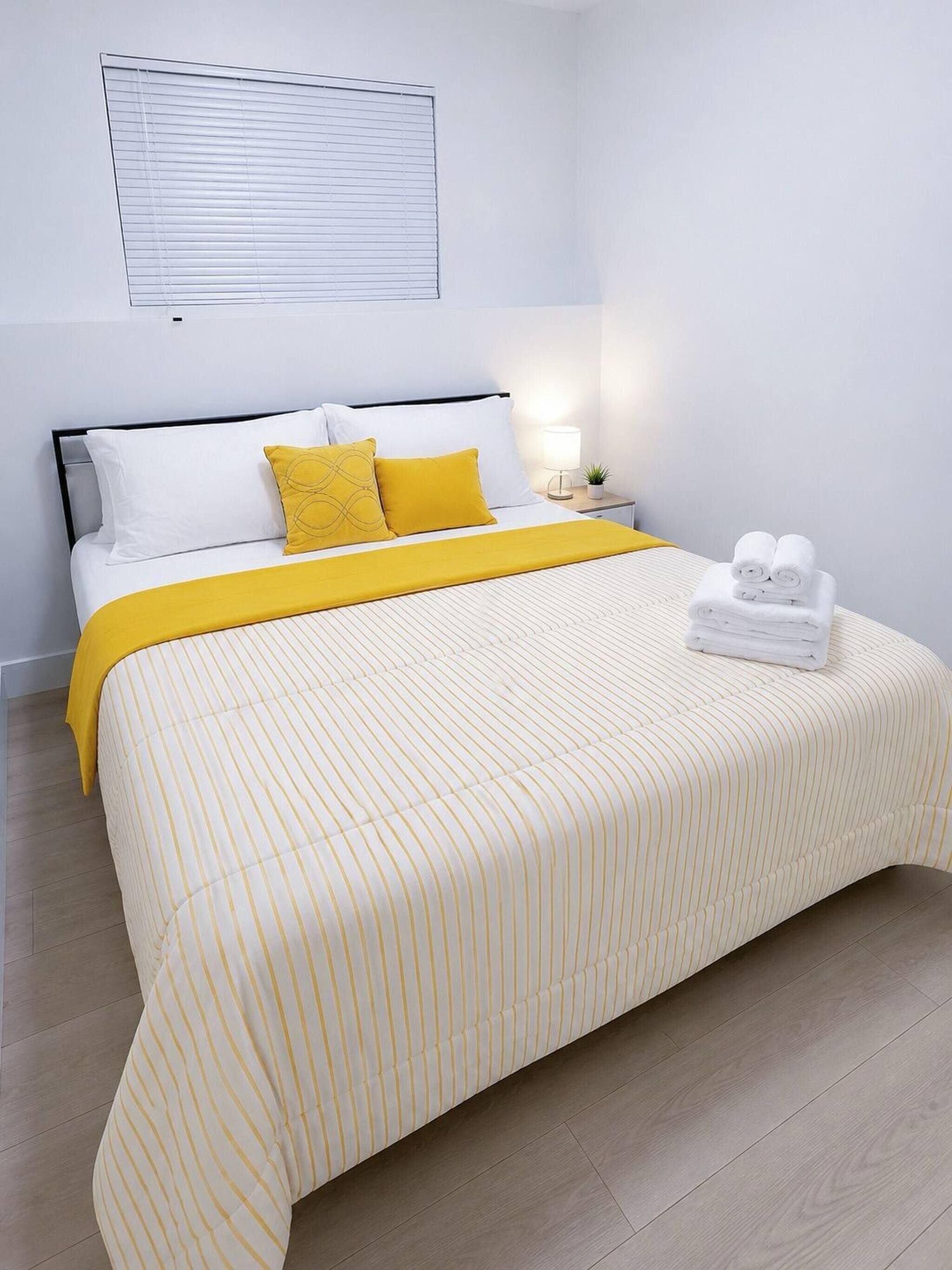 A neatly made bed with a striped bedspread, a bedside lamp, and a small plant on the nightstand.
