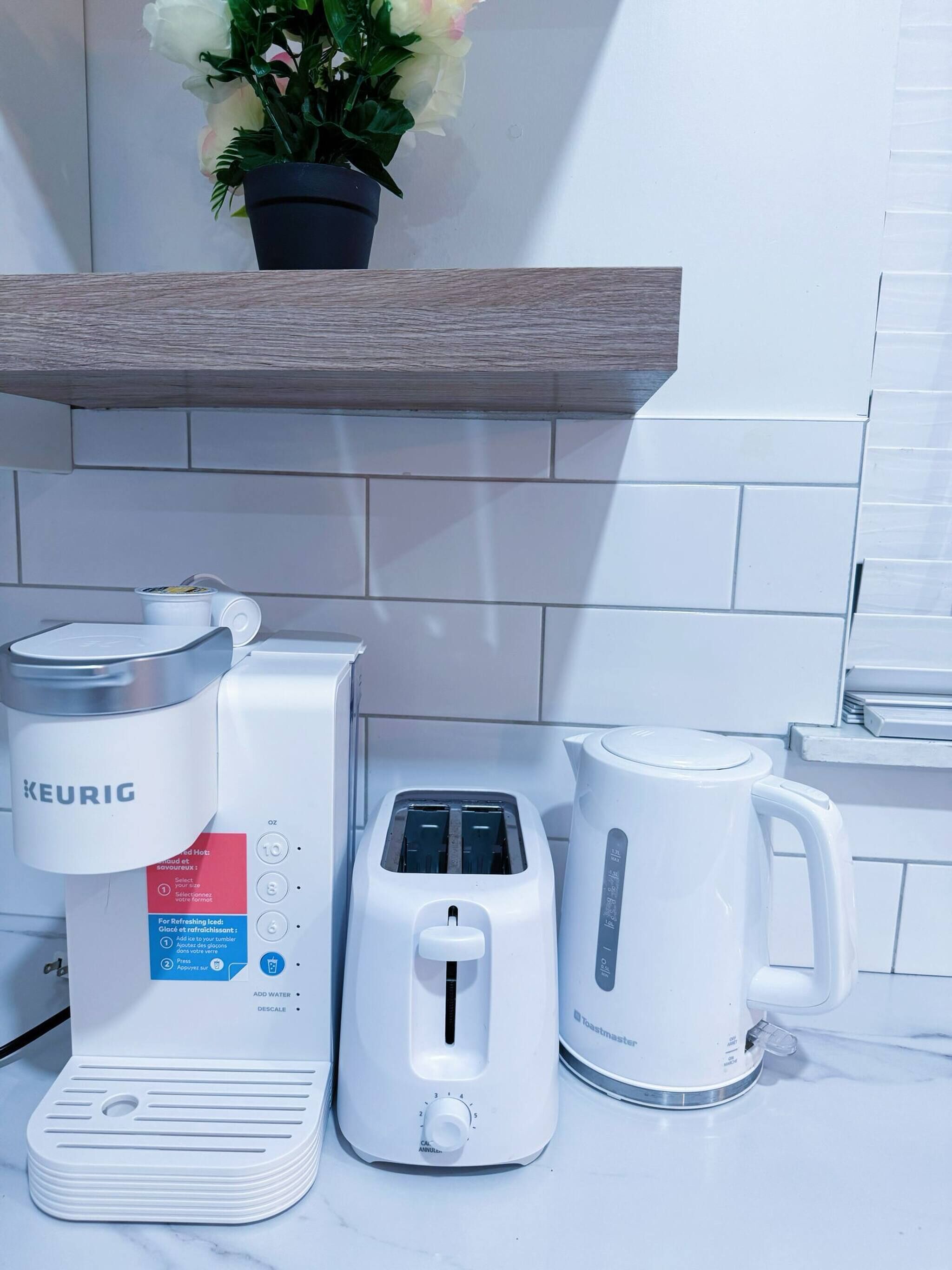 Eine Küchenzeile mit einer Keurig-Kaffeemaschine, einem Toaster und einer Kaffeekanne auf einer weißen Arbeitsplatte.