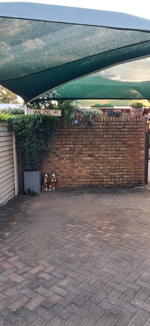 A brick wall with a green mesh shade, a potted plant, and a sign reading 'VAN ZYL AVE.' - Luxury guest Apartment Fully furnished with all amenities (Pretoria)