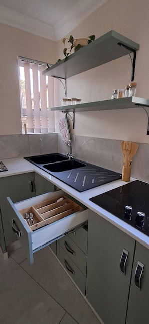 A kitchen with a built-in sink, a countertop with a wooden utensil holder, and a window with blinds. - Luxury guest Apartment Fully furnished with all amenities (Pretoria)