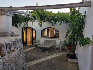 A courtyard with a table and chairs, arched doorways, and a pergola covered with vines. - Authentic trulli centrally in Valle d'Itria (Ceglie Messapica)