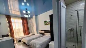 A hotel room with two beds, a desk, a shower, and a painting on the wall. - Hotel Mimino & Restaurant (Batumi)