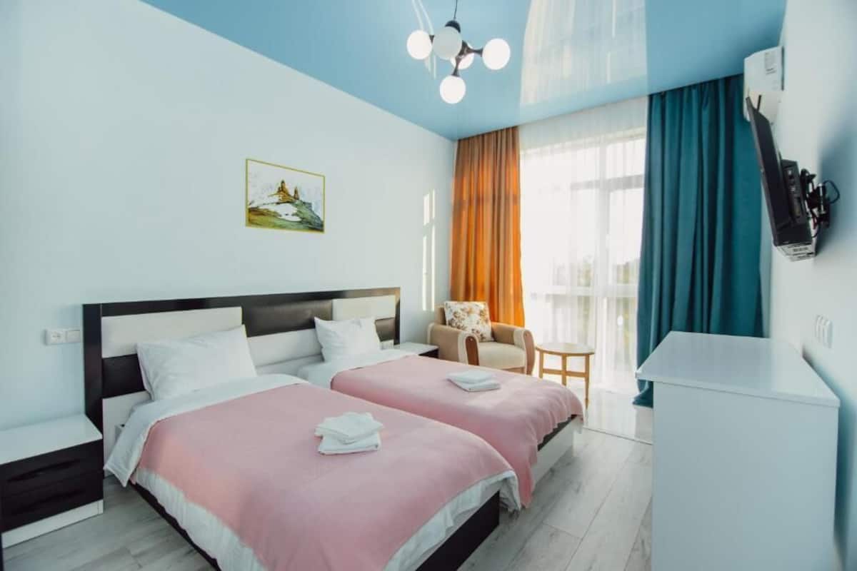 Ein Hotelzimmer mit zwei Betten, einem Schreibtisch, einem Stuhl, einem Fernseher und einem Bild an der Wand.