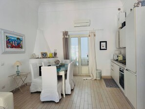 Un espace de vie compact comprenant un coin repas, une kitchenette et un balcon agrémenté de rideaux.
