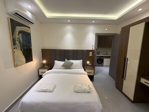 Et moderne hotelværelse med en stor seng, sengeborde med lamper, et garderobeskab og udsigt til et køkkenområde.