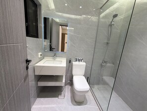 Et moderne badeværelse med et glas brusekabine, en hvid vask og et toilet.